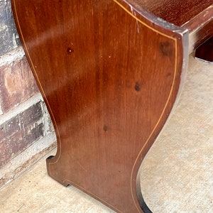 May include: A wooden bench with a curved back and a simple design. The bench is made of dark wood with a light wood inlay around the edges.