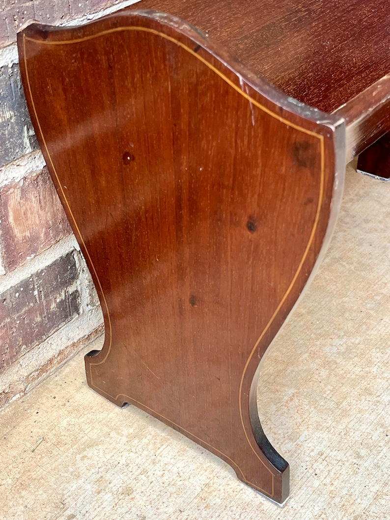 May include: A wooden bench with a curved back and a simple design. The bench is made of dark wood with a light wood inlay around the edges.