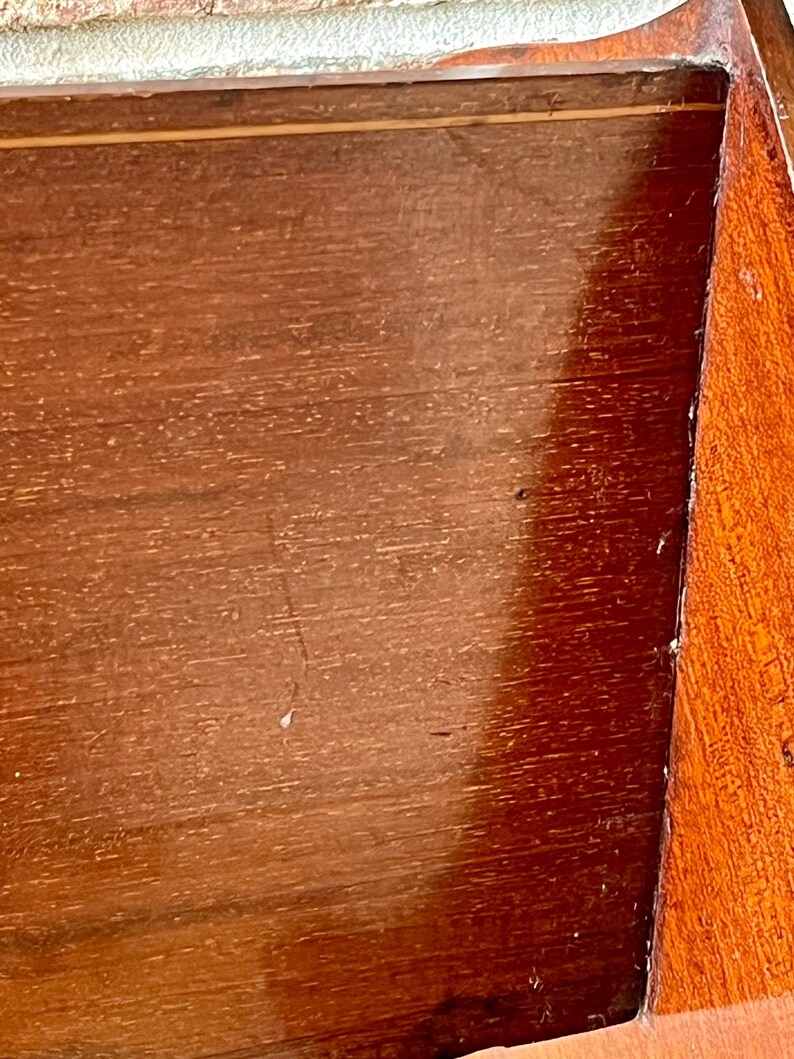 May include: Close-up of a wooden surface with a light brown finish. The surface has a smooth, polished look with a subtle grain pattern. The wood appears to be part of a box or cabinet.