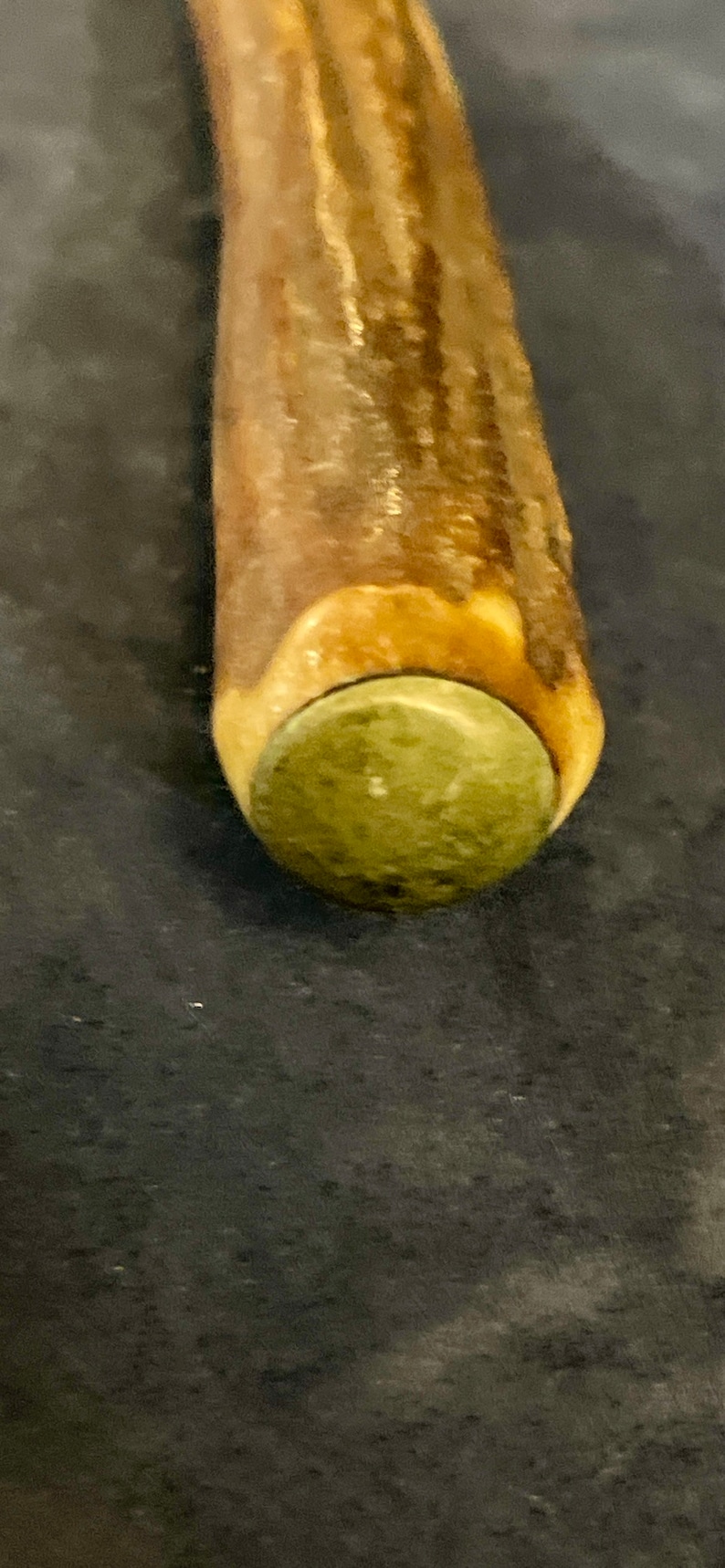 May include: Close-up of a wooden walking stick with a brown and green antler handle.