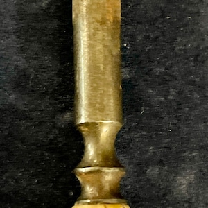 May include: A close-up of a vintage, metal and wood handled tool. The handle is made of a light brown wood with a dark brown stain. The metal part of the tool is silver and has a decorative design.