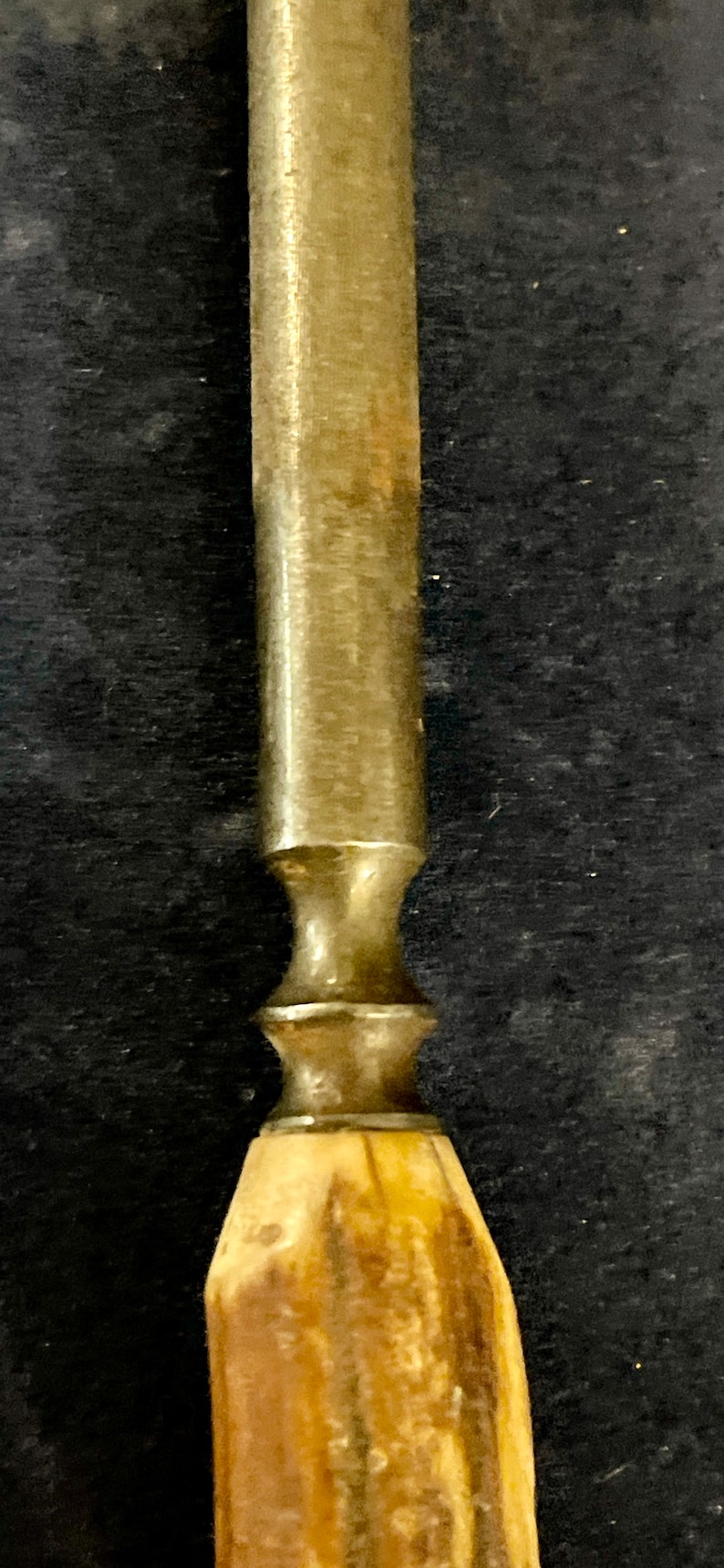 May include: A close-up of a vintage, metal and wood handled tool. The handle is made of a light brown wood with a dark brown stain. The metal part of the tool is silver and has a decorative design.