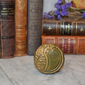 May include: A vintage brass door knob with an ornate design. The knob is a deep green color and has a raised, floral pattern.