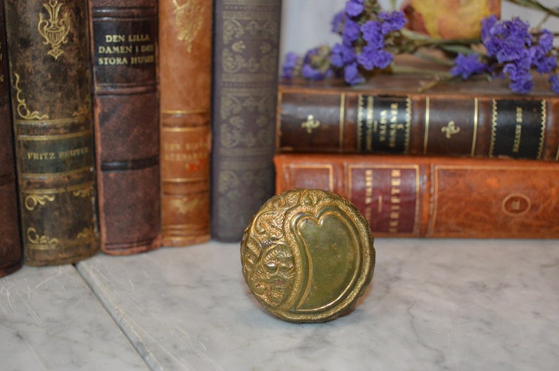 May include: A vintage brass door knob with an ornate design. The knob is a deep green color and has a raised, floral pattern.