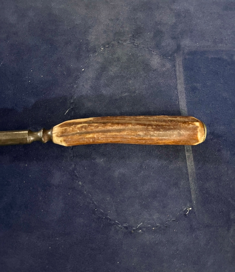 May include: A close-up of a brown antler handle attached to a metal knife blade. The knife is lying on a blue surface.