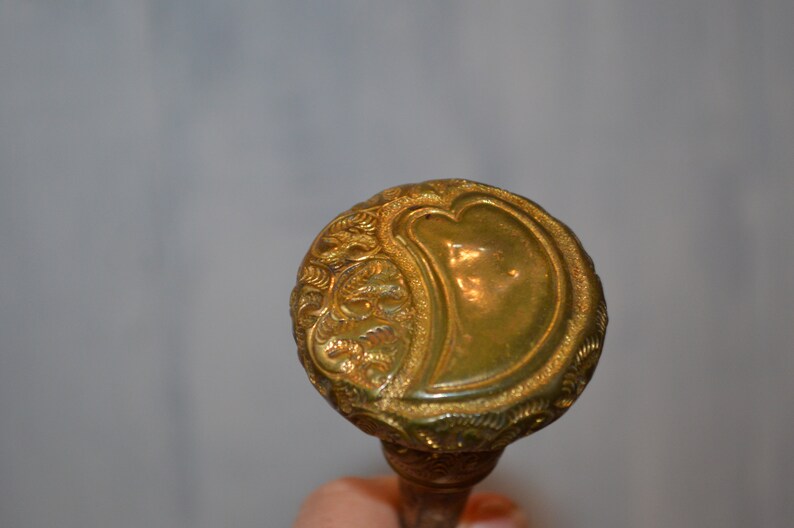 May include: A gold-colored walking stick handle with an ornate design featuring a heart shape.