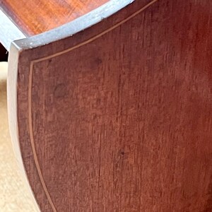 May include: Close-up of a wooden table top with a curved edge and a decorative inlay. The wood is a rich brown color and has a natural grain pattern.