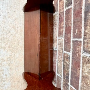 May include: A dark brown wooden bench with a simple design. The bench has a rectangular top and four legs. The legs are shaped like a V at the bottom.