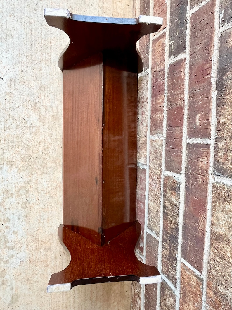 May include: A dark brown wooden bench with a simple design. The bench has a rectangular top and four legs. The legs are shaped like a V at the bottom.