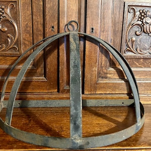 May include: A semi-circular metal frame structure featuring a dark, weathered finish. The object consists of a horizontal base band connected to a series of curved vertical ribs that meet at a central circular loop at the top of the dome.