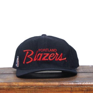 Puede incluir: Gorra de béisbol negra con un logotipo bordado en rojo "Portland Blazers".