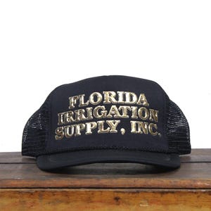 Pode incluir: Boné de caminhoneiro preto de malha com um logotipo bordado em ouro que diz "FLORIDA IRRIGATION SUPPLY, INC."
