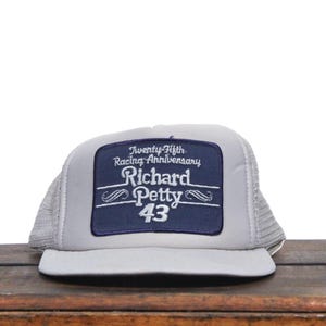 May include: A gray and blue trucker hat with a patch that says "Twenty-Fifth Racing Anniversary Richard Petty 43".