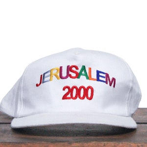 以下が含まれることがあります： 虹色の刺繍で「JERUSALEM 2000」と刺繍された白い野球帽