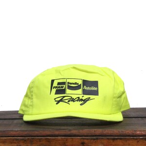 May include: A neon yellow baseball cap with black text that reads "FRAM, Bendix, Autolite, Racing".