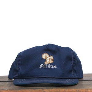 May include: A navy blue baseball cap with a brown squirrel embroidered on the front. The cap has the text "Mill Creek" embroidered below the squirrel.