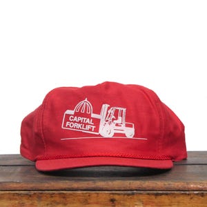 May include: Red baseball cap with a white logo of a forklift and the text "CAPITAL FORKLIFT".