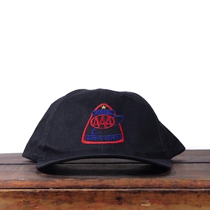 May include: Black baseball cap with a red, blue, and gold embroidered patch. The patch features the text "SCHOOL SAFETY PATROL" and the AAA logo. The cap is sitting on a wooden surface.