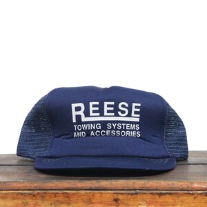 May include: A blue and black mesh trucker hat with the white text "REESE TOWING SYSTEMS AND ACCESSORIES".