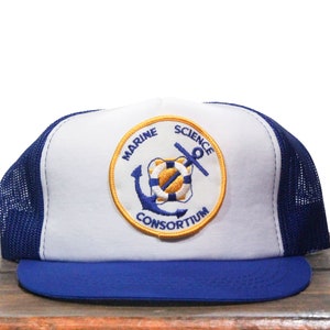 Puede incluir: Gorra de camionero blanca y azul con un parche bordado amarillo y azul que dice "Marine Science Consortium" y presenta un ancla y un salvavidas.