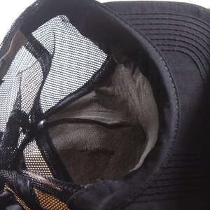 May include: Black trucker hat with a mesh back and a structured front. The hat's interior is visible, showing a worn, gray lining. The brim is curved, and the hat appears to be made of durable fabric.