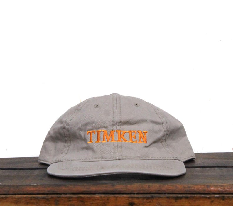 Puede incluir: Una gorra de b&eacute;isbol gris con un logotipo bordado en naranja que dice "TIMKEN".