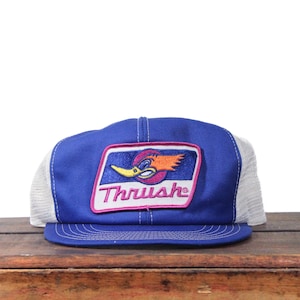 May include: A blue and white trucker hat with a patch featuring a cartoon bird and the word "Thrush" in a pink and white rectangle. The hat has a blue front panel and a white mesh back.