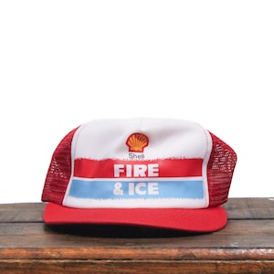 Op de afbeelding: Een rode, witte en blauwe truckercap met een Shell-logo en de woorden "Fire & Ice" op de voorkant.