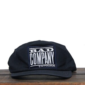 May include: Black baseball cap with a white embroidered patch that says "BAD COMPANY" with a small copyright symbol and the text "1980 AFTERGLOBE, INC."