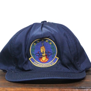 Puede incluir: Una gorra de béisbol azul marino con un parche bordado que presenta una llave inglesa amarilla, una mano roja y el texto "5TH MAINTENANCE SQ".