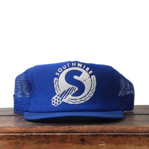 May include: A blue trucker hat with a white embroidered logo that reads "SOUTHWIRE". The hat has a curved brim and a mesh back. The logo features a stylized "S" and a graphic element.