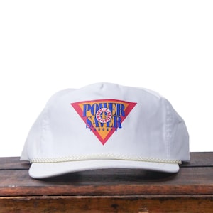 May include: White baseball cap with a flat brim and a rope detail. The cap features a colorful logo with the words "POWER SAVER PROGRAM" in a red, yellow, blue, and purple design. The cap is sitting on a wooden surface.