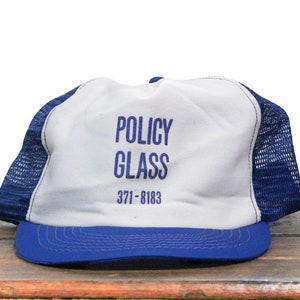 Puede incluir: Una gorra de camionero blanca y azul con el texto "POLICY GLASS 371-8183" bordado en azul.