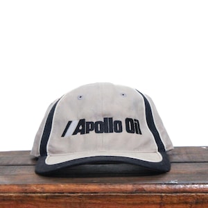 Op de afbeelding: Een beige baseballpet met zwarte bies en de tekst "Apollo Oil" in zwart geborduurd op de voorkant.