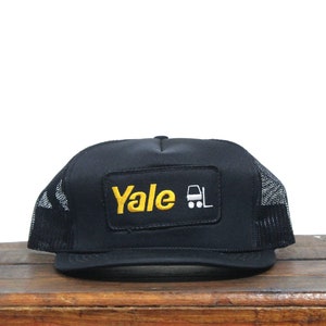 May include: Black trucker hat with a yellow patch that says "Yale" and a white forklift icon.