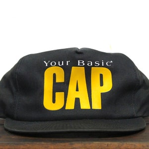 May include: Black baseball cap with a yellow "Your Basic CAP" logo.