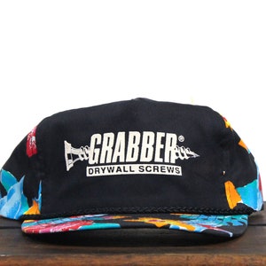 Puede incluir: Una gorra de béisbol negra y azul con un estampado floral colorido en la visera. La parte delantera de la gorra tiene un logotipo blanco que dice "Grabber Drywall Screws" con una imagen de tornillo estilizada.