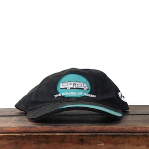 May include: Black baseball cap with a teal trim and a circular patch. The patch features a white camper van design inside a teal circle, with the text "THE POWER OF GREEN".