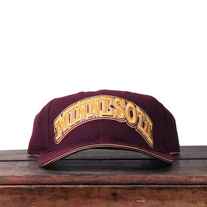 May include: A maroon baseball cap featuring the word "MINNESOTA" in gold, arched across the front. The cap has a yellow trim and a structured design.