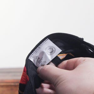 Puede incluir: Gorra de b&eacute;isbol negra con detalles rojos y amarillos. La gorra tiene una visera curva y una etiqueta con el texto "CAT CATERPILLAR". La gorra est&aacute; siendo sostenida por una persona.