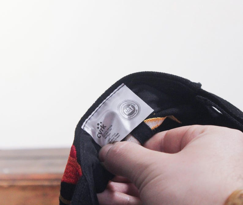 Puede incluir: Gorra de b&eacute;isbol negra con detalles rojos y amarillos. La gorra tiene una visera curva y una etiqueta con el texto "CAT CATERPILLAR". La gorra est&aacute; siendo sostenida por una persona.