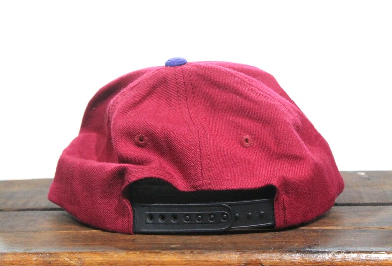 May include: A maroon baseball cap with a black strap and a small blue patch on the top.