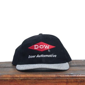 May include: A black and grey baseball cap with a red diamond logo that says "DOW" and the text "Dow Automotive" embroidered on the front.