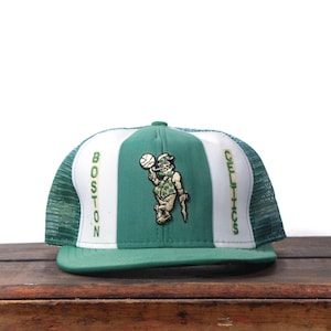 Puede incluir: Gorra de camionero de los Celtics de Boston verde y blanca. La gorra presenta el logotipo del equipo en la parte delantera, con la palabra "BOSTON" en el lado izquierdo y "CELTICS" en el lado derecho. La gorra tiene una parte trasera de malla y una visera curva.