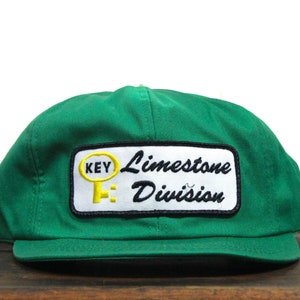 May include: Green trucker hat with a white patch that says "KEY Limestone Division" in black lettering. The key is yellow.