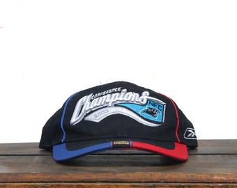 May include: Black baseball cap with "Conference Champions 2003" embroidered on the front. The cap features a blue and red brim, with a Carolina Panthers logo and the NFL logo. The Reebok logo is on the side.