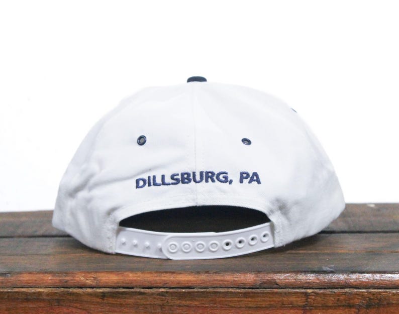K&ouml;nnte beinhalten: Wei&szlig;e Baseballkappe mit einem marineblauen Schirm und einem marineblauen gestickten Logo mit der Aufschrift "Dillsburg, PA".