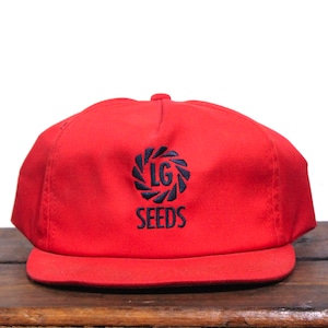 May include: A red baseball cap with a black embroidered logo that says "LG SEEDS" with a stylised design of a circle with a swirl inside.