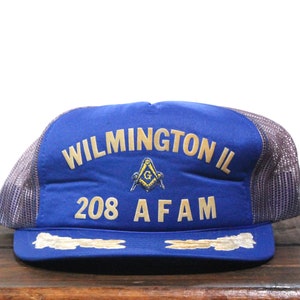 Puede incluir: Gorra de camionero azul y gris con el texto "WILMINGTON IL 208 AFAM" y un símbolo masónico dorado.