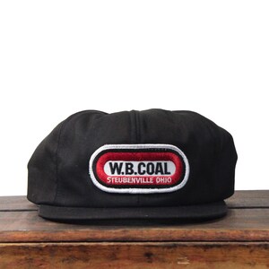 May include: Black baseball cap with a flat brim. The cap features a rectangular patch with the text "W.B. COAL" in white letters on a red background, outlined in white. Below the text is "STEUBENVILLE OHIO".